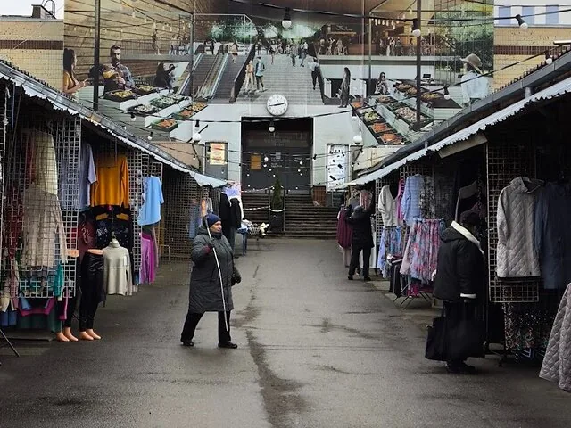 Une femme traverse un marché de plein air couvert avec des stands de vêtements.