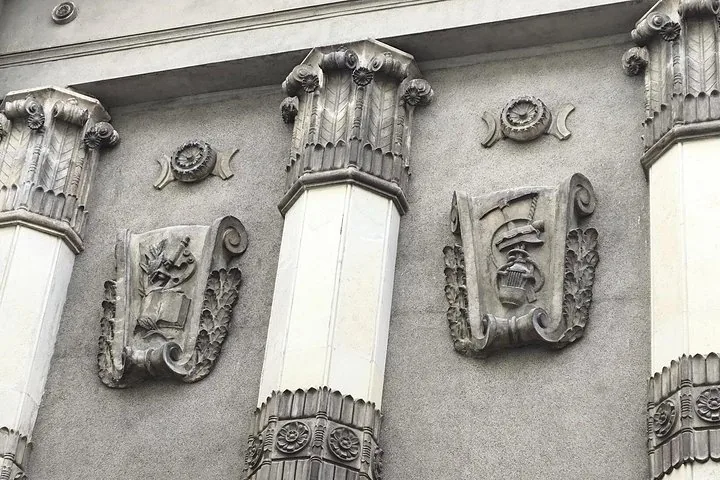 Gros plan de reliefs en pierre représentant un microscope et des outils industriels sur un bâtiment.